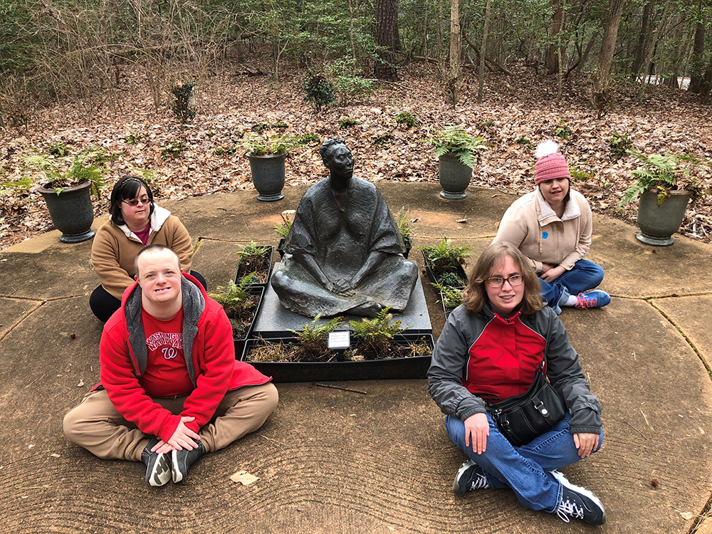 A group of people sitting on the ground in front of a statue.